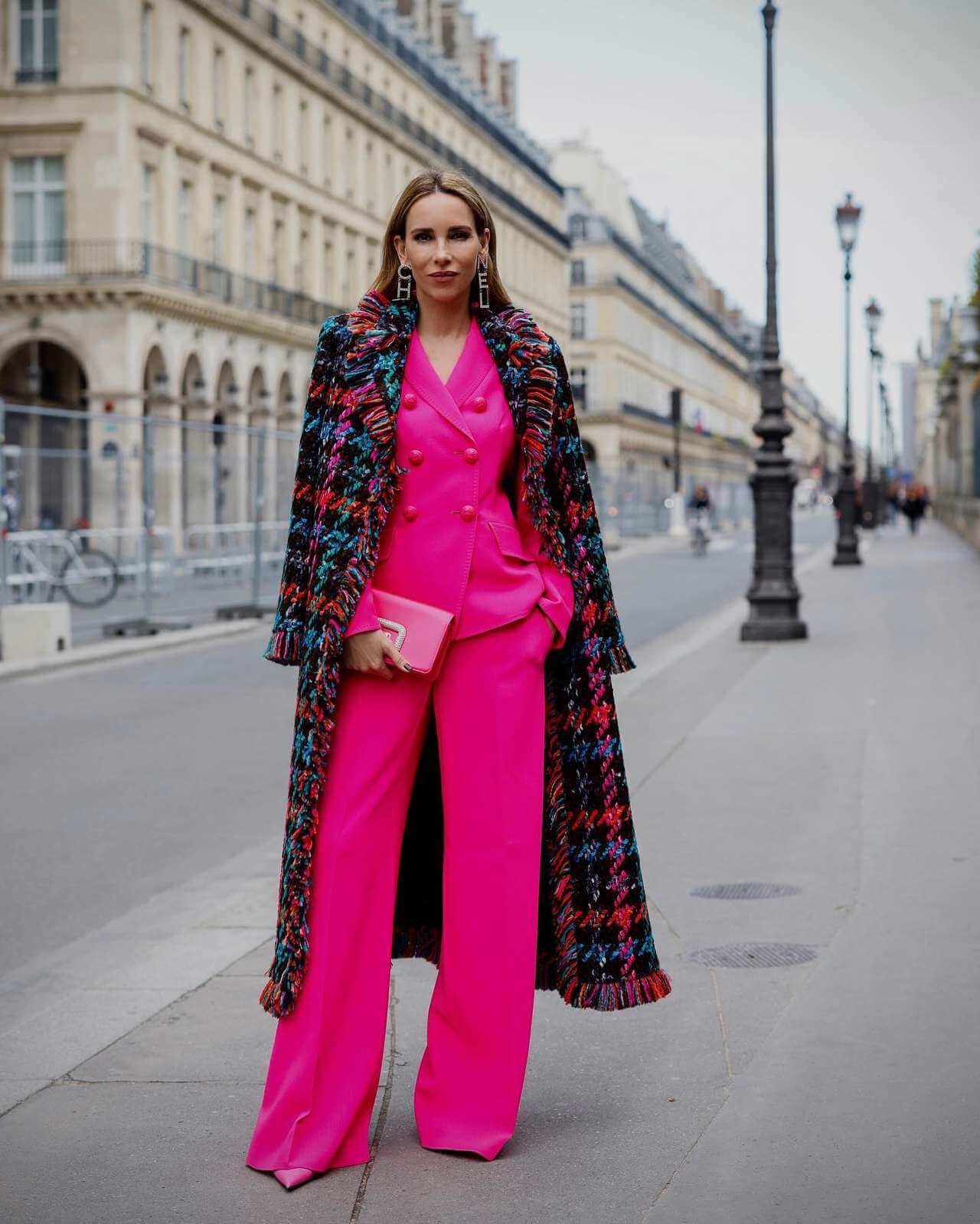 Foto de mujer luciendo una blusa fuxia, pantalon fuxia, bolso fuxia, tacones fuxias y un abrigo de colores